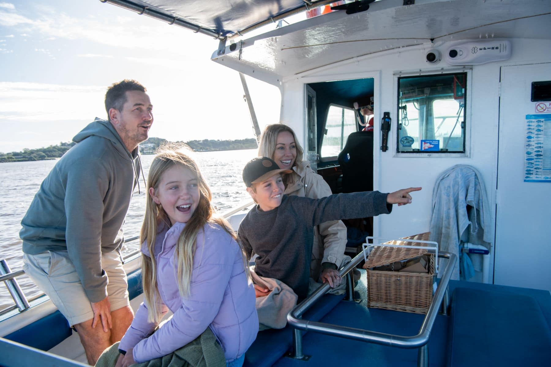 A smiling family on board a Fozies Fishing Adventures charter boat in Ballina, enjoying a day out on the Richmond River as a young boy points excitedly.