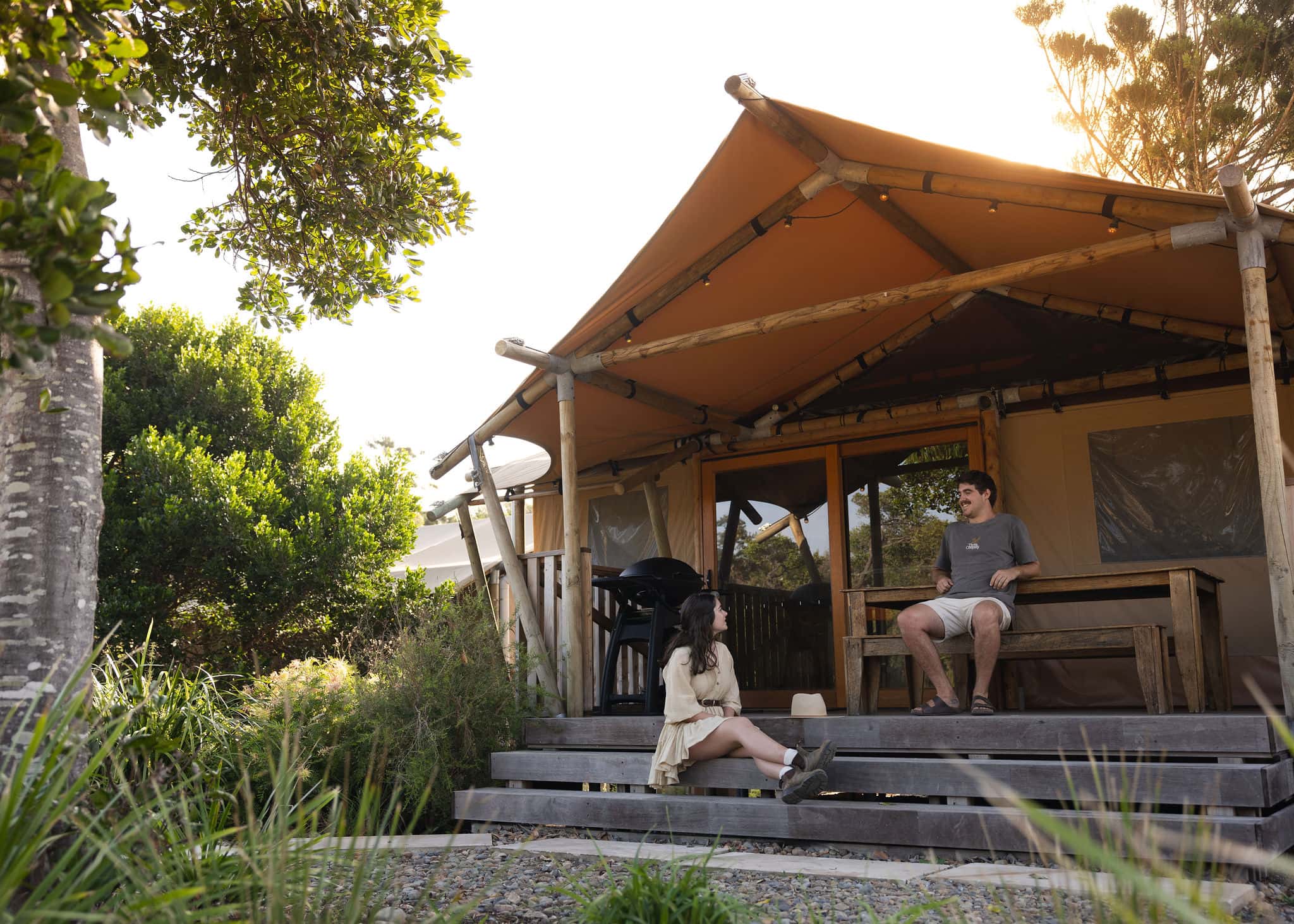 Couple relaxing outside a luxury glamping safari tent at Ballina Beach Nature Resort, surrounded by coastal bushland and native greenery.