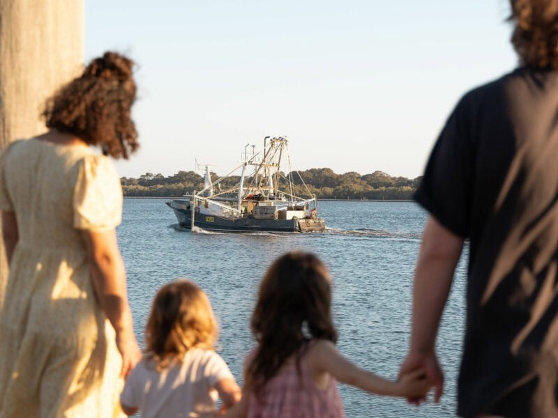 Family watching a prawn trawler depart on the Richmond River in Ballina, Northern NSW