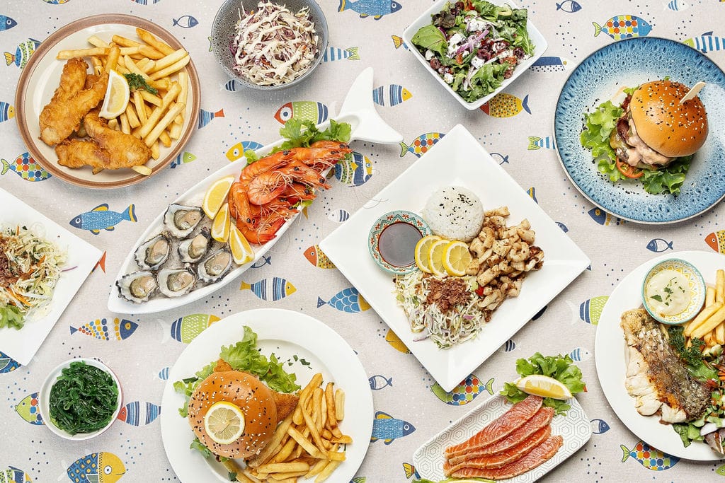 Seafood spread at Fishy Fishy Restaurant Lennox Head featuring oysters, prawns, fish and chips, burgers, and salads on a colourful coastal tablecloth