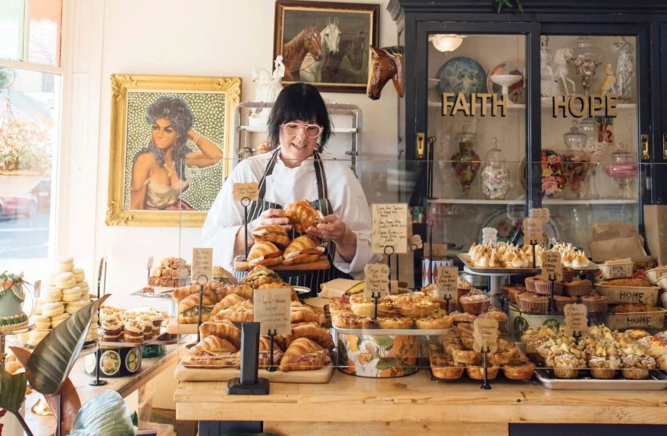Smiling baker behind a counter full of croissants, tarts and pastries at Home Alstonville.