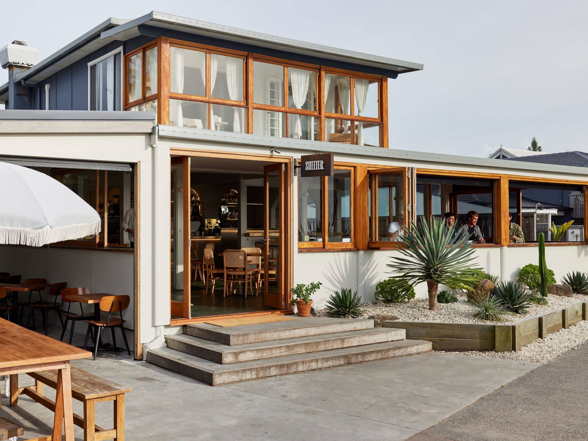 Exterior of Shelter restaurant in Lennox Head, with modern coastal design, outdoor seating, and desert-style landscaping.