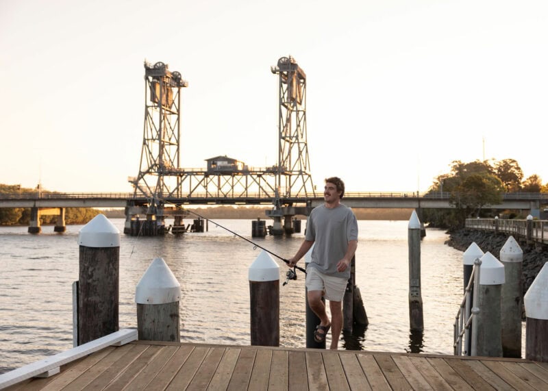 Man fishing at the Wardell Wharf on the Richmond River with the historic Wardell lift bridge in the background at sunset.