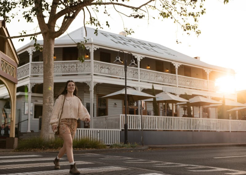 A young woman walking across a pedestrian crossing in front of the historic Federal Hotel in Alstonville at sunset.