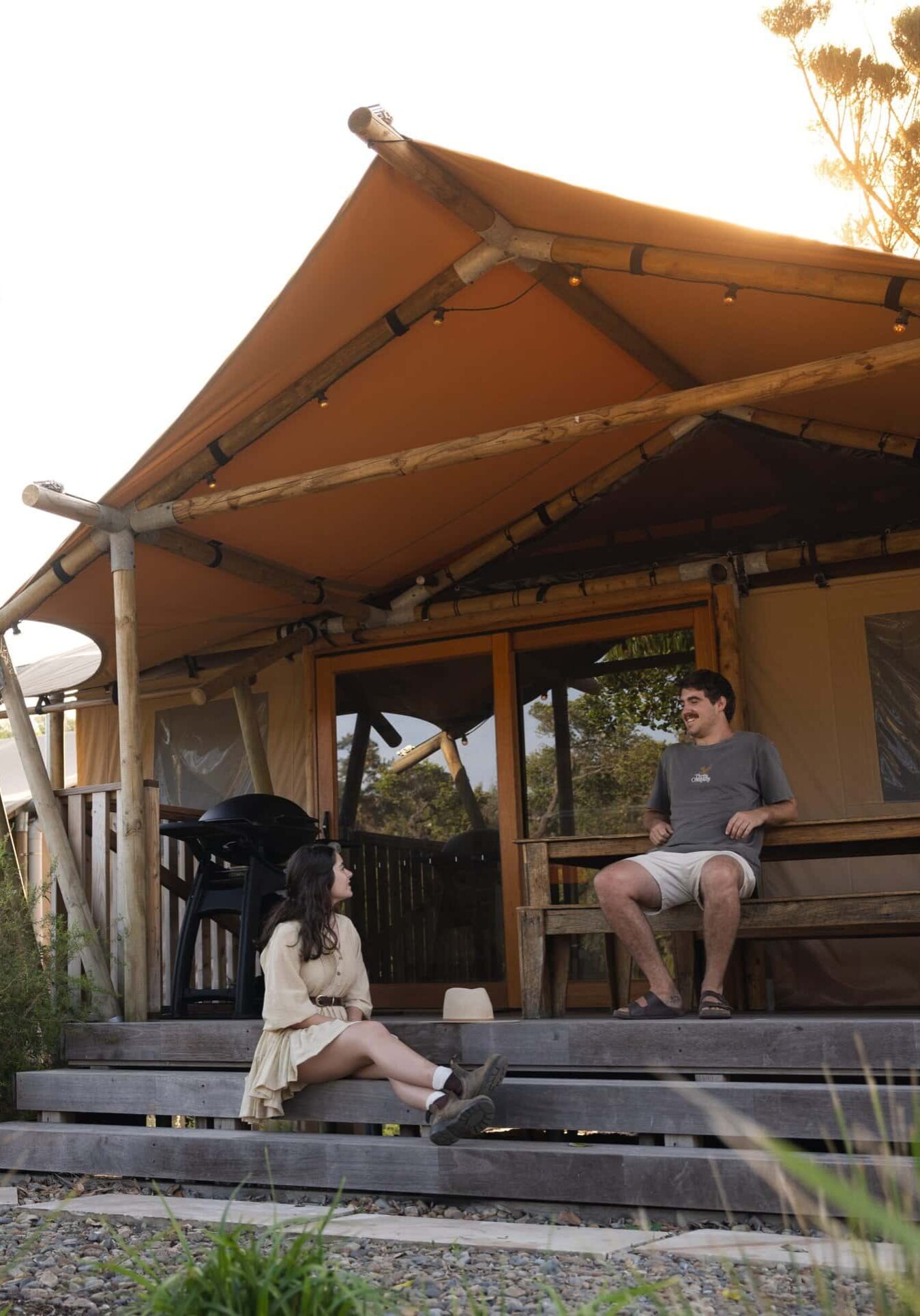 Couple relaxing outside a luxury glamping tent at Ballina Beach Nature Resort in South Ballina, surrounded by native bushland and coastal greenery.