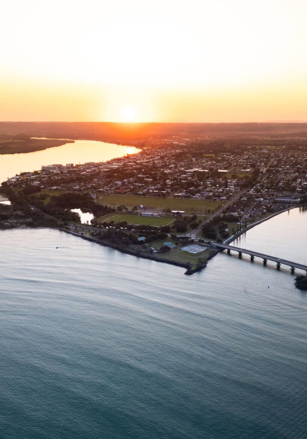Aerial view of Ballina, NSW at sunset showing the Richmond River, coastline, and townscape bathed in golden light.