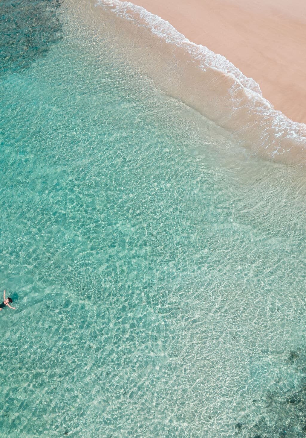 Aerial view of two people floating in crystal-clear turquoise water near a pristine Boat Channel in Lennox Head, NSW