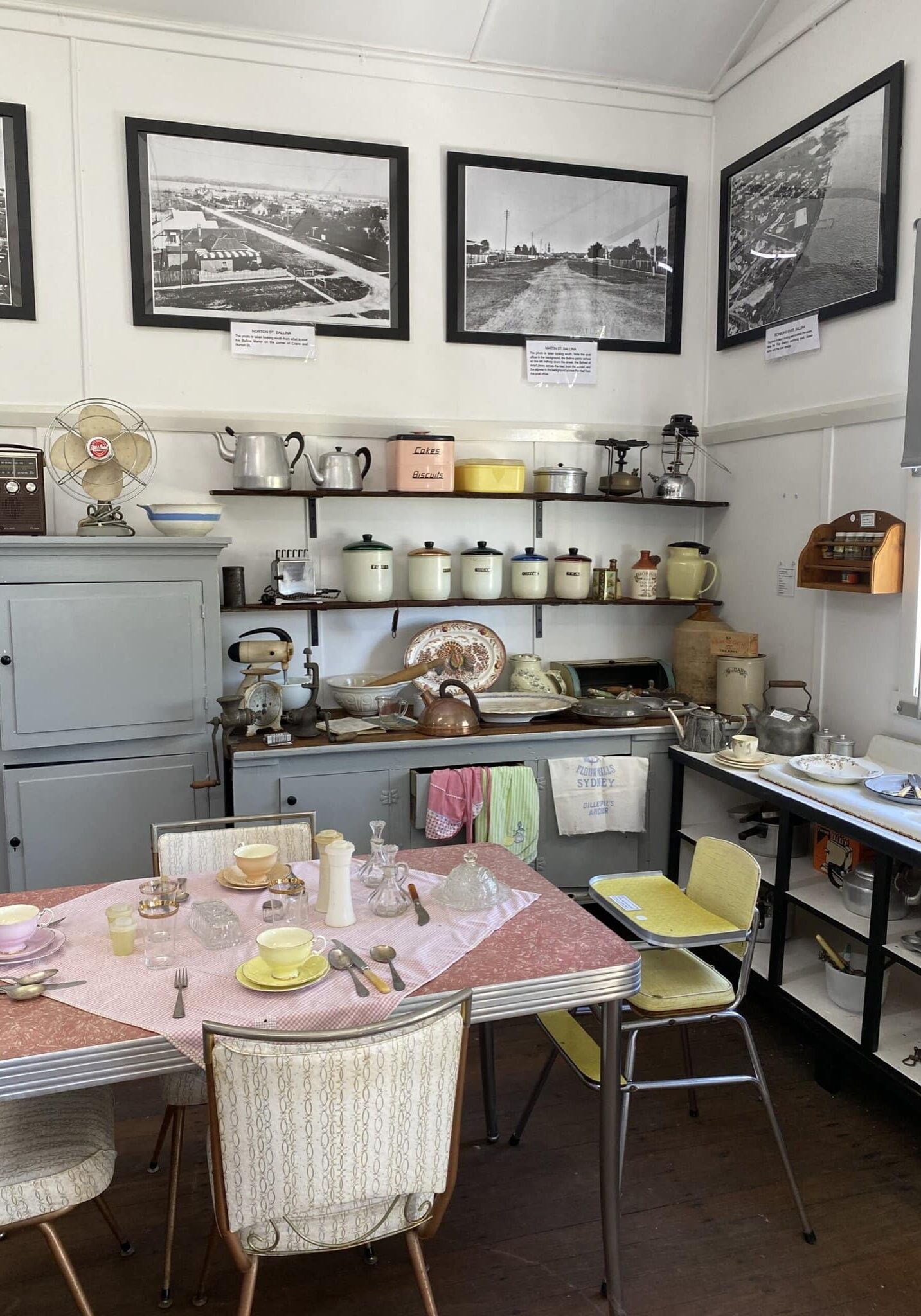 Vintage kitchen exhibit at the Ballina District Historical Museum, featuring 20th-century crockery, appliances, utensils, and black-and-white photographs on the wall.