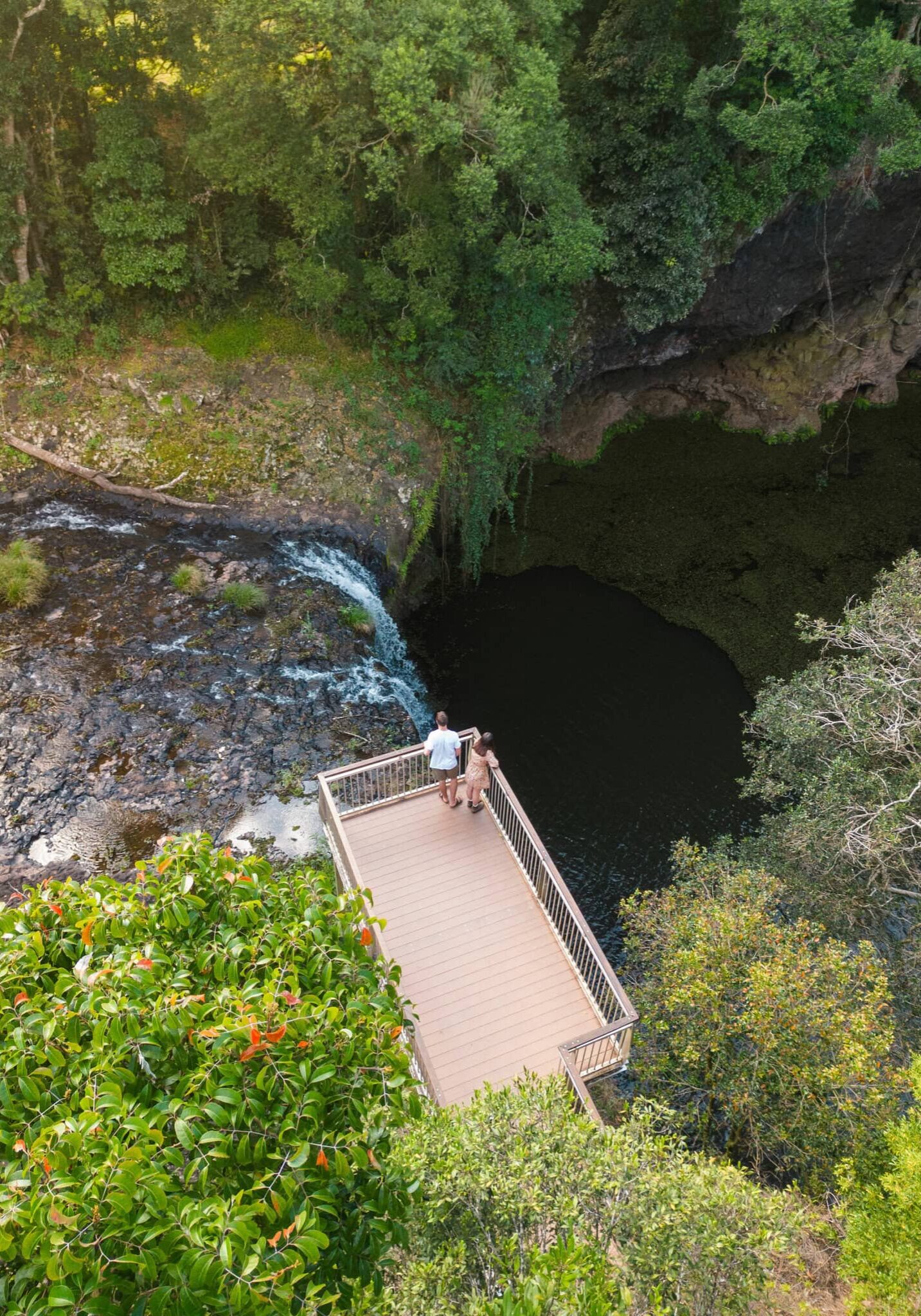 Couple standing on Killen Falls lookout platform overlooking waterfall and plunge pool in the lush Ballina Hinterland, Northern NSW
