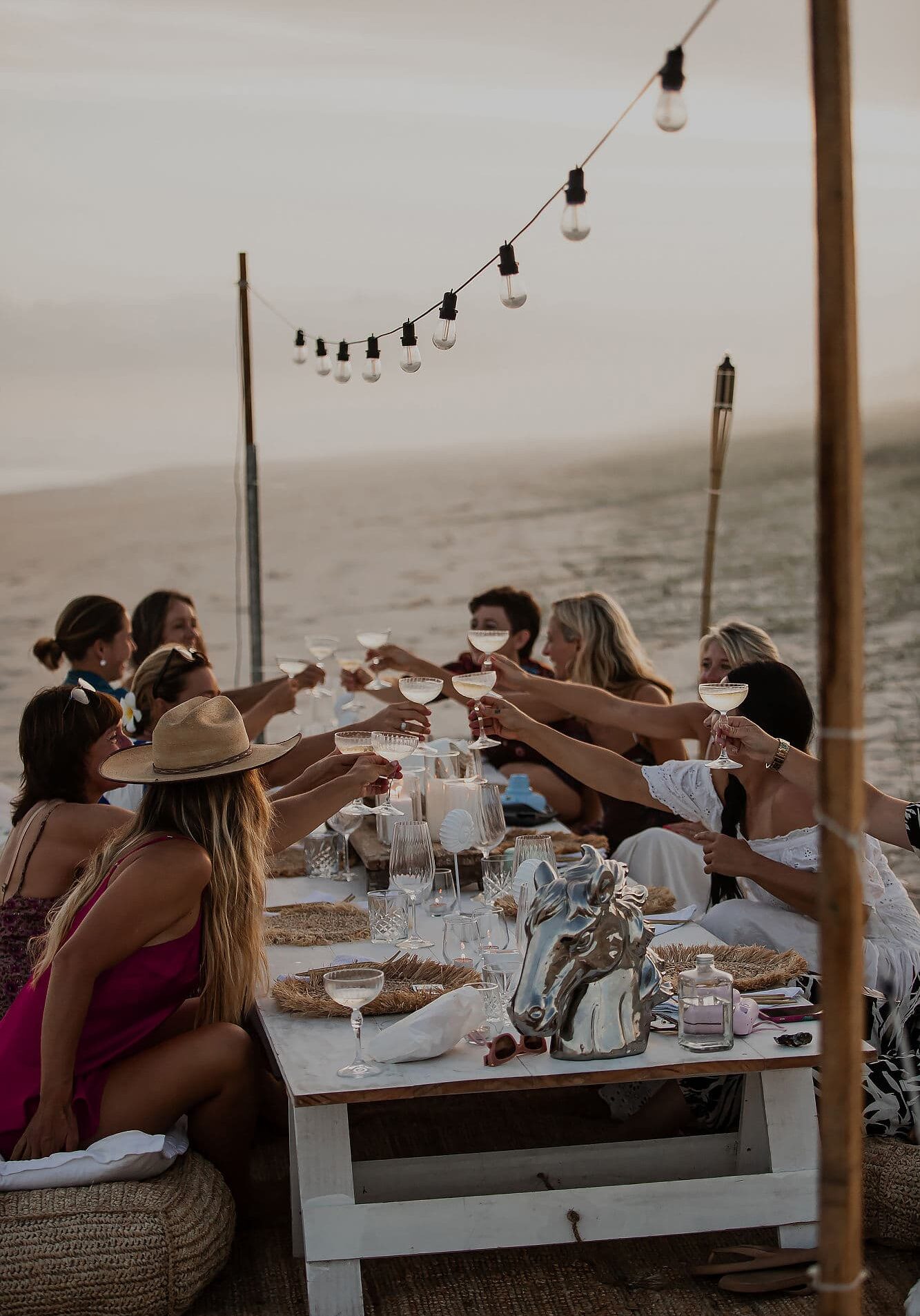 Group of women enjoying a sunset toast at an outdoor beachfront table during a Sugar Beach Ranch retreat in South Ballina, New South Wales.