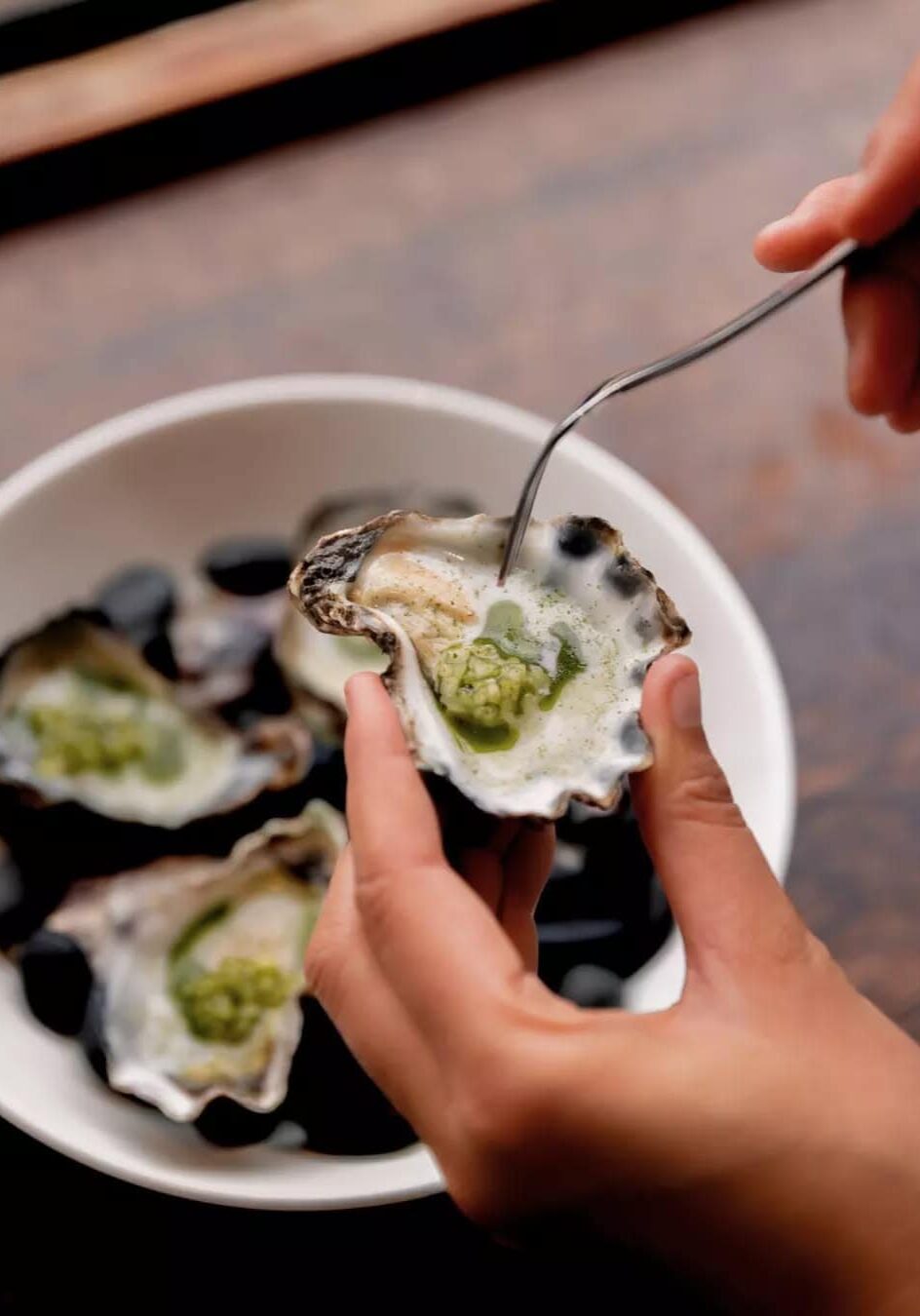 Close-up of a hand holding a freshly shucked oyster topped with green garnish at Shelter restaurant in Lennox Head.