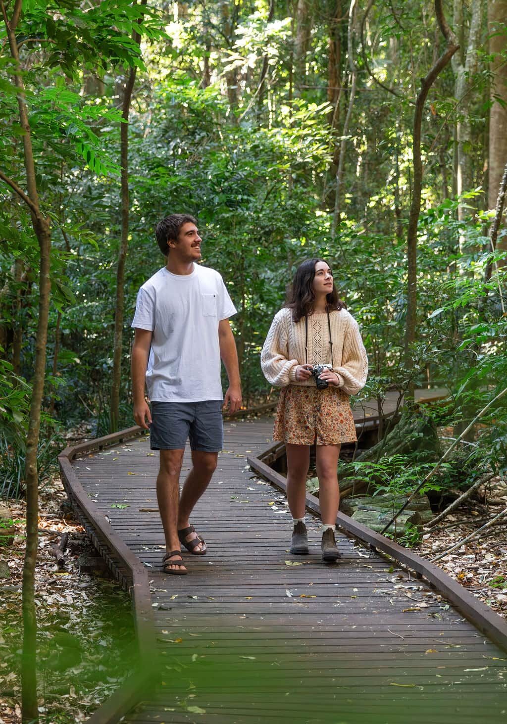 A young couple walking along a timber boardwalk through lush subtropical rainforest at Victoria Park Nature Reserve, near Alstonville.