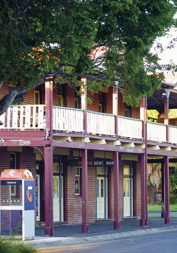 Historic two-storey red brick pub with wraparound verandah and vintage Telstra phone box in Wardell, NSW.